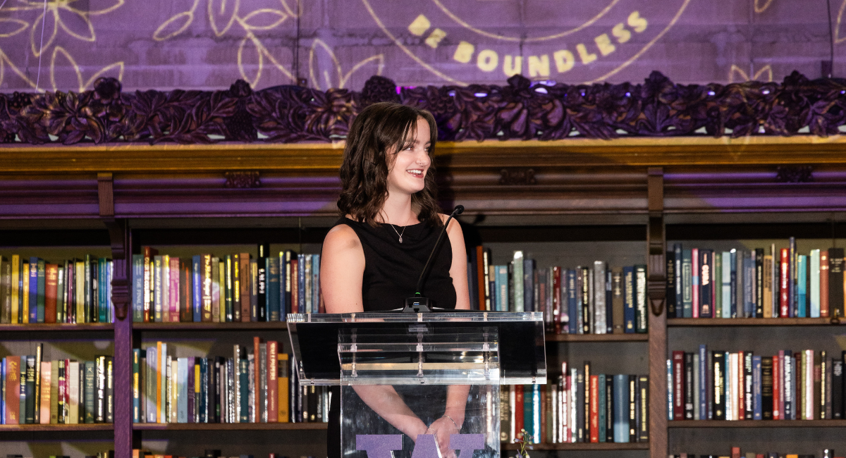 Cordy stands at podium surrounded by books