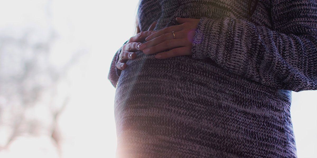 Pregnant woman in sweater resting hands on belly, backlit by the sun - Pexel Images